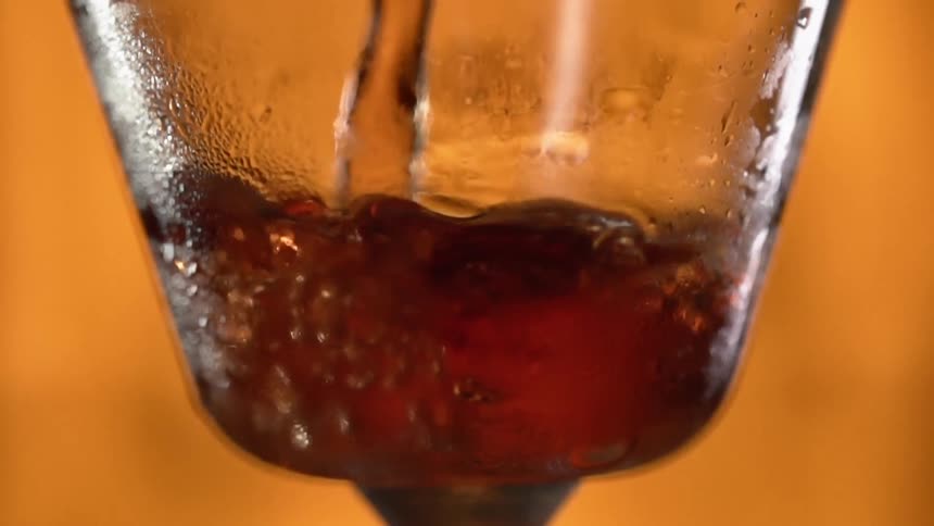 Brown liquid is being poured into a glass