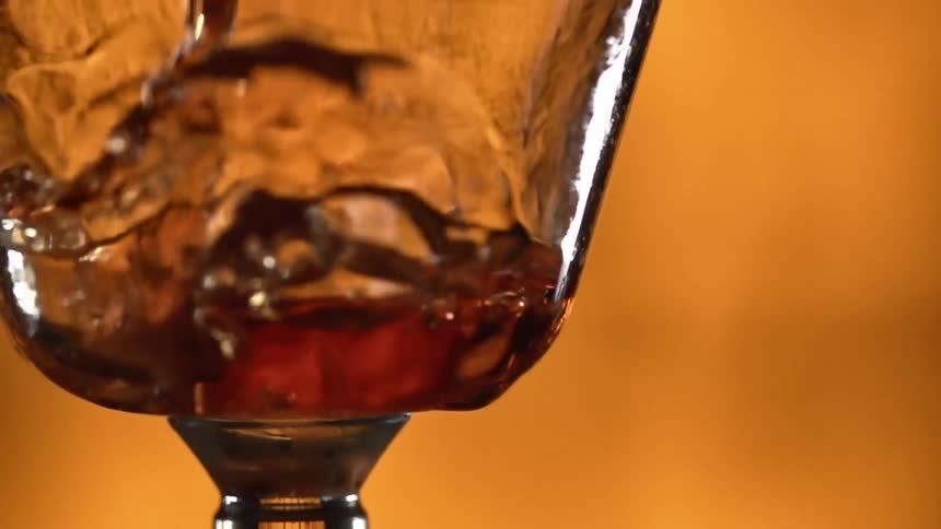 Red wine being poured in a glass cup on a yellow background