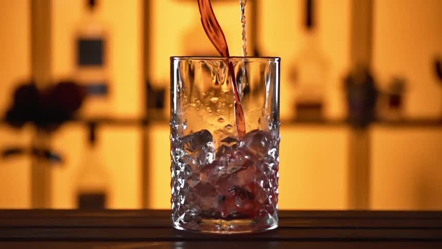 Cocktail pouring over ice in a glass at a bar counter