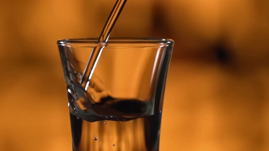 Clear liquor pouring in a small glass shot against a yellow background