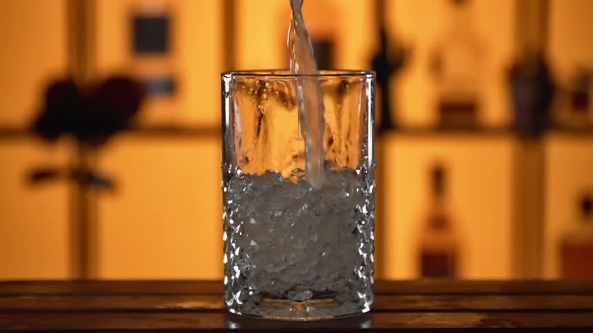 A drink is being poured into a glass on a counter in a bar