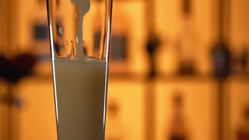 A thick yellowish white liquid is being poured into a glass in a bar