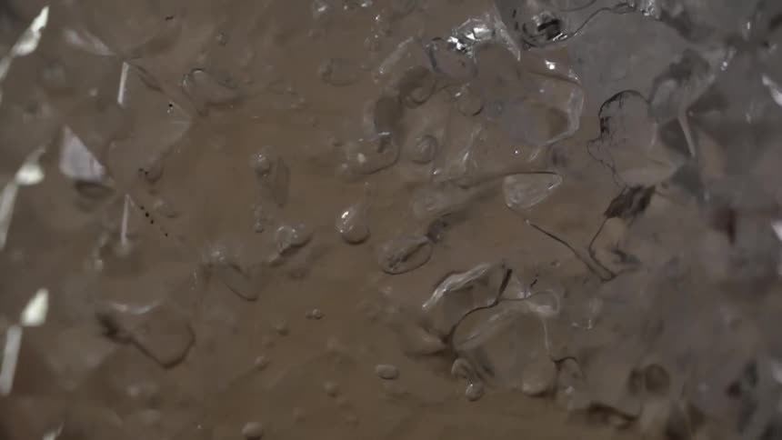 A yellow tinted liquid is poured over crushed ice and slowly flows downward through the ice