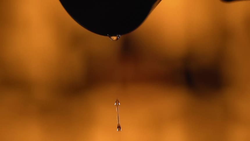 Black gloved hand pours liquid from a metal container into a glass
