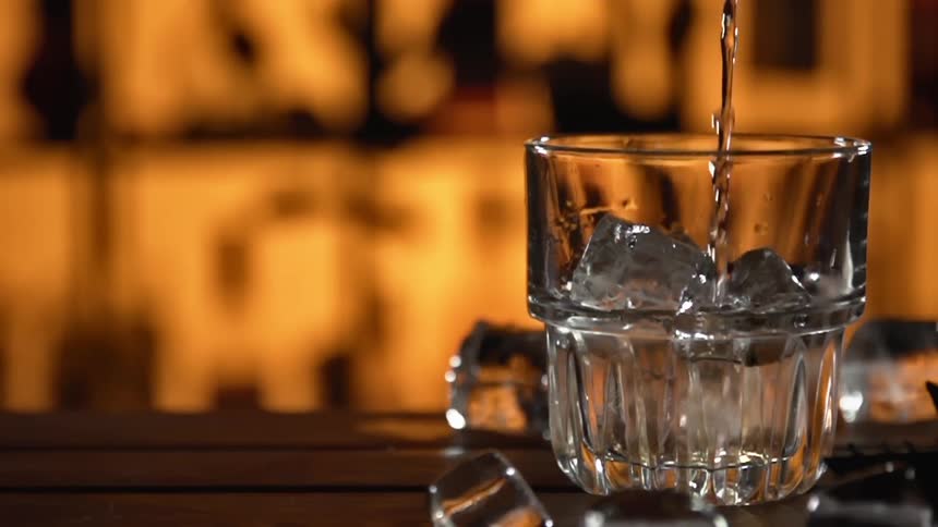 Alcohol pouring over ice in a glass at bar counter