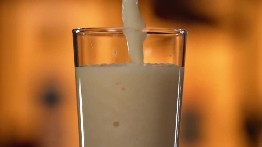 A pale colored shake being poured into a drinking glass