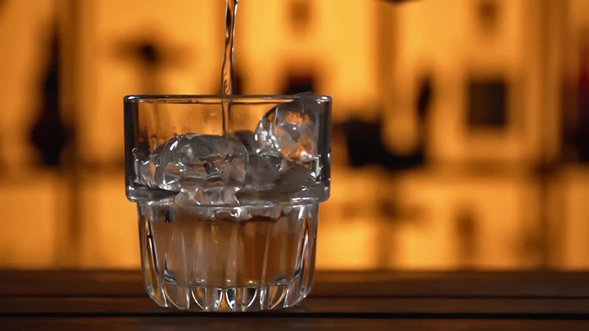 Clear liquor pouring over the ice inside a glass over the counter