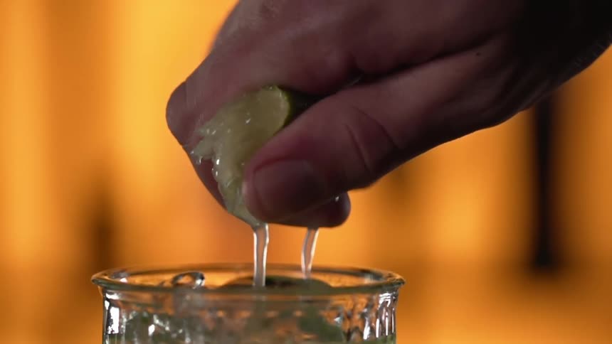 Man squeezes a fresh lemon into a glass with ice cubes