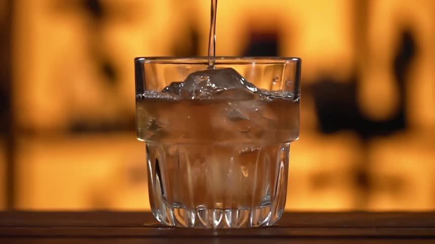 A liquid is being poured into a glass with ice cubes