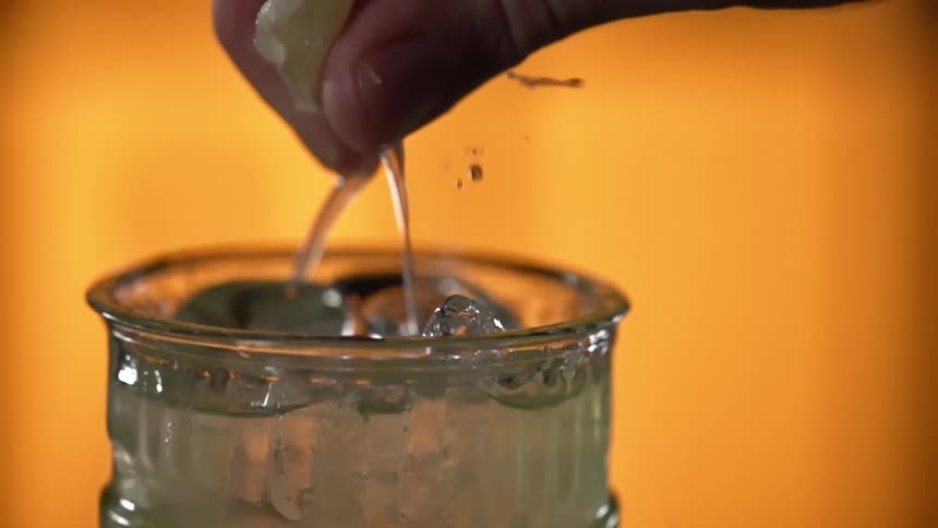 Close up of a man squeezing a fresh lemon into a glass with ice cubes
