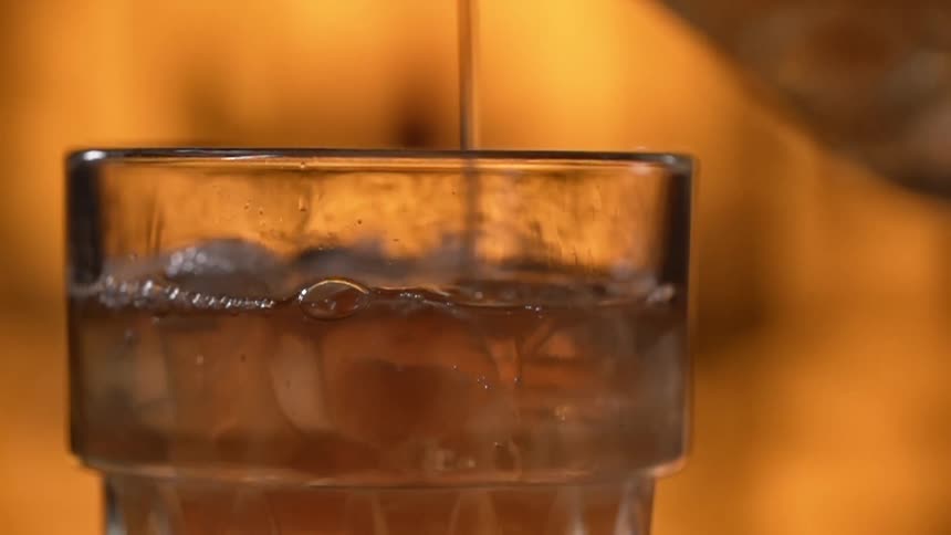 Liquid is being dropped into a glass with ice cubes in a bar