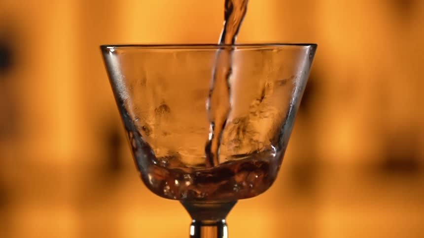 Red liquid is poured into a glass in a bar