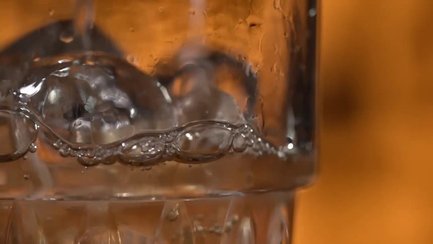 Liquid being poured into a glass with ice cubes at a bar