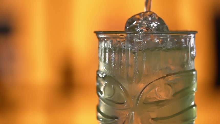 Liquid is being poured into a glass with ice cubes