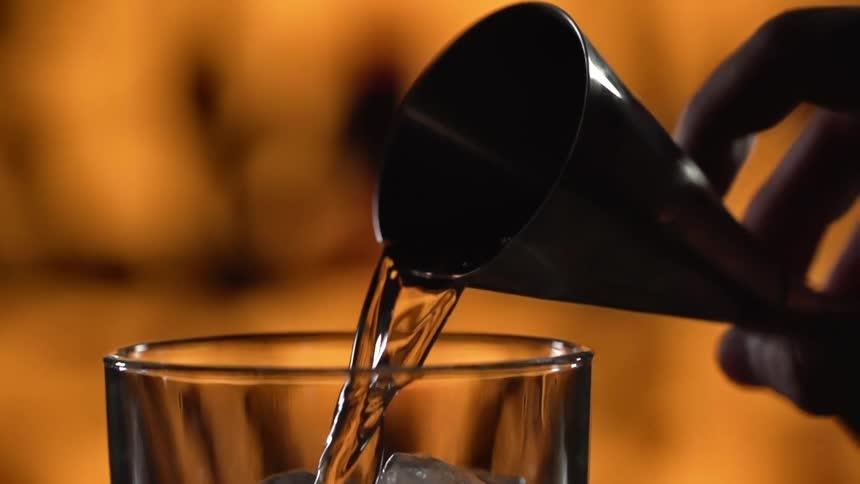 Person pours clear liquid onto ice in glass from cone