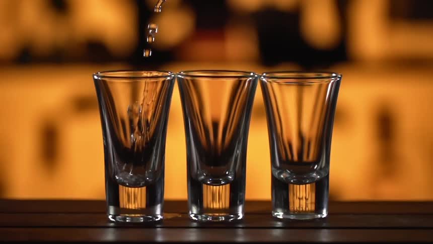 Clear liquor pouring on glass shots over a bar