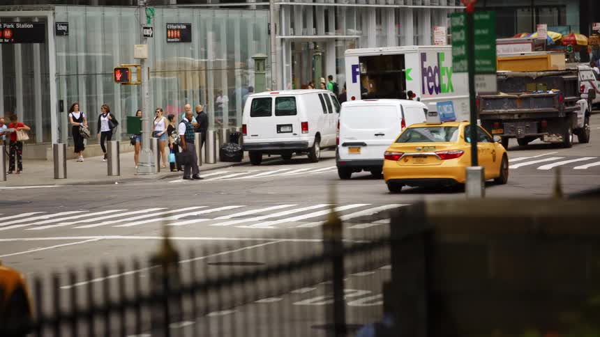 Pedestrians wait at zebra crossing to cross the road while vehicles driving on the road