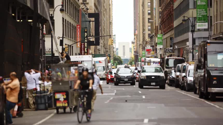 A bicyclist pedals along a busy downtown street lined with vendors and filled with several vehicles