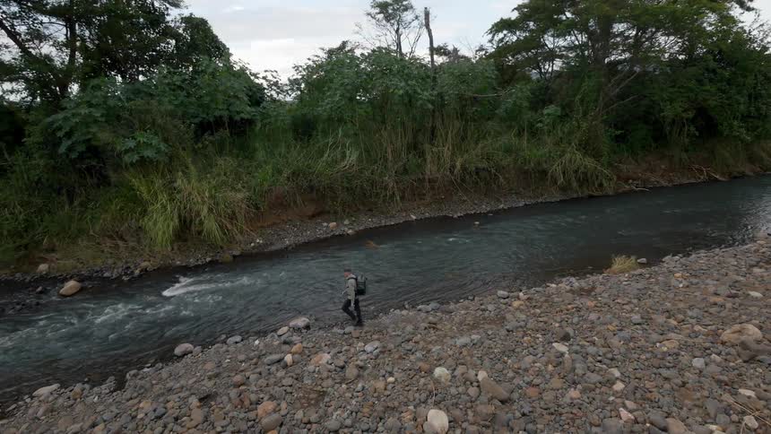 A man is hiking along a stream on a cloudy day
