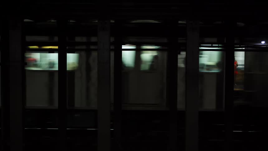 A subway station with a train running by with people inside and on the platform in the background