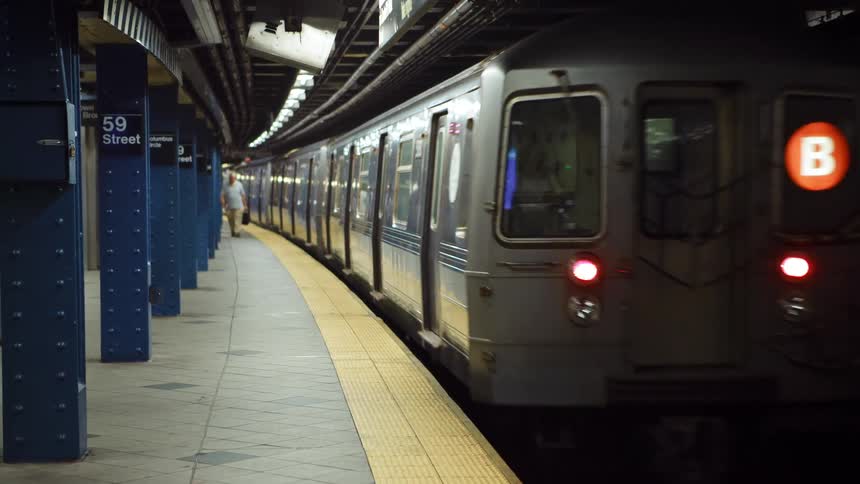 Male and female walking quickly along the 59th street subway platform as the train moves away in the opposite direction