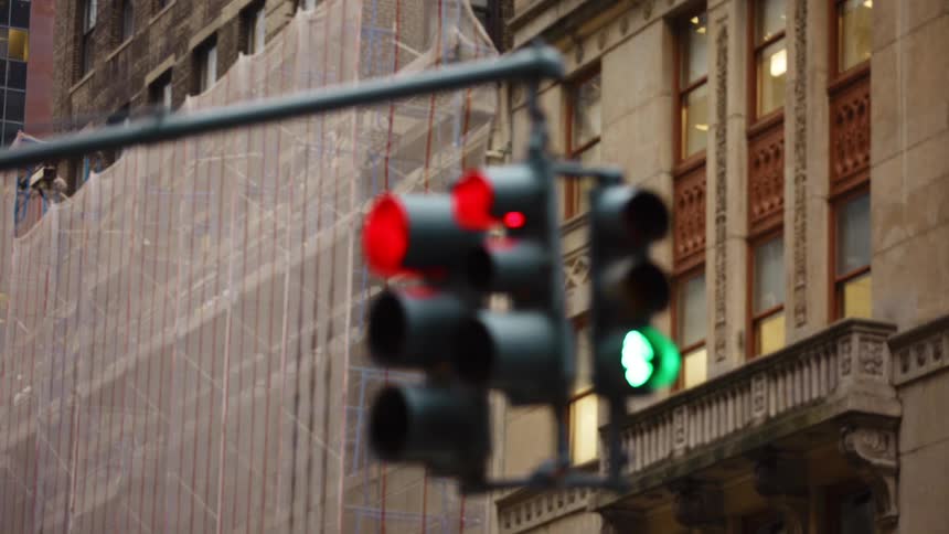 A hanging street light going from green to red at an intersection in a metropolis