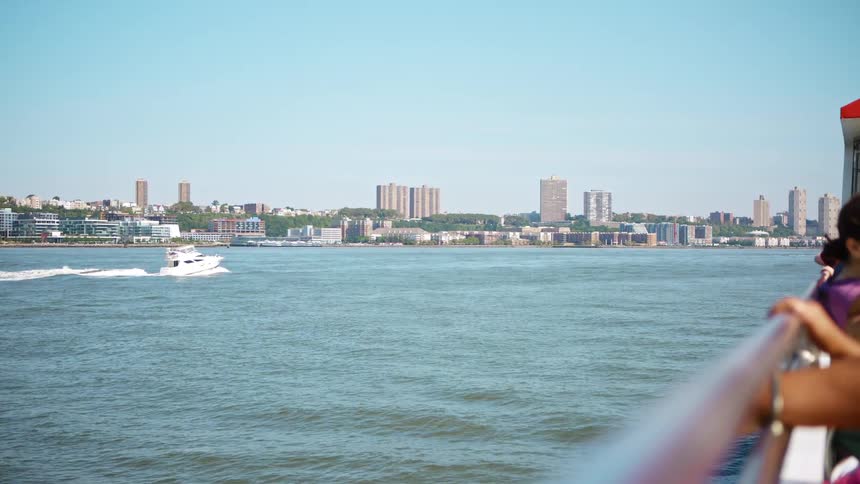 People hold onto the railing of a ferry as it goes through the water near a city