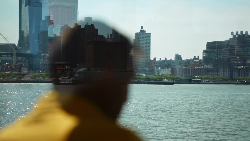 Rear view of a male passenger watching a big city skyline as traveling by a ferry across a river