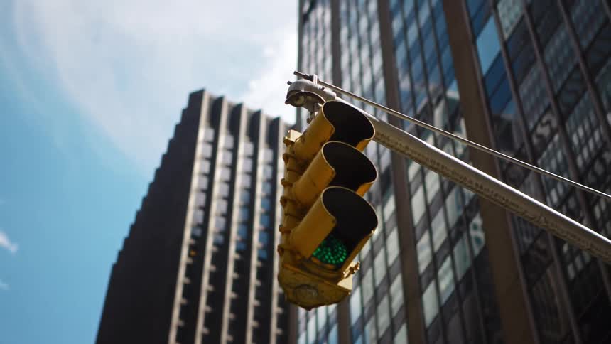 A hanging traffic light at an intersection below a row of skyscrapers in a metropolis