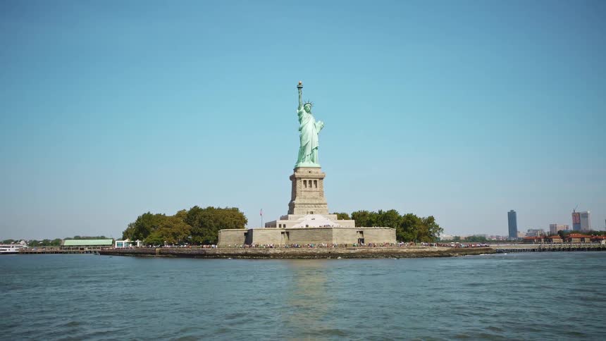 The statue of liberty with city buildings behind on a bright blue sky day
