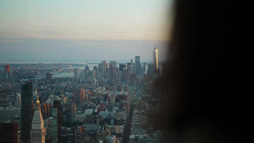 Rear view of a woman looking out the high rise office window at a big city skyline with tall buildings and skyscrapers on the horizon at dusk