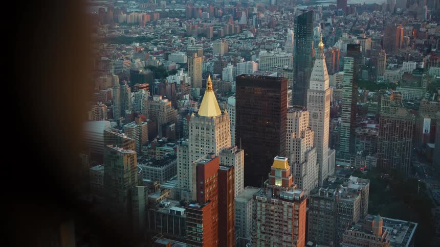 Rear view of a woman looking out the high rise office window at a big city skyline with tall buildings and skyscrapers on the horizon at dusk