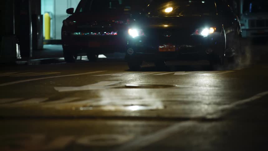 Steam rises up from manhole covers as cars travel on a city street at night