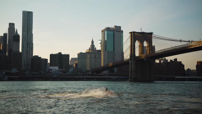 Person on a jet ski passes under the brooklyn bridge in new york