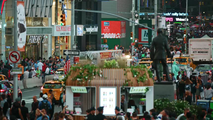 Cars drive down a busy city street lined with stores as people flood the sidewalks