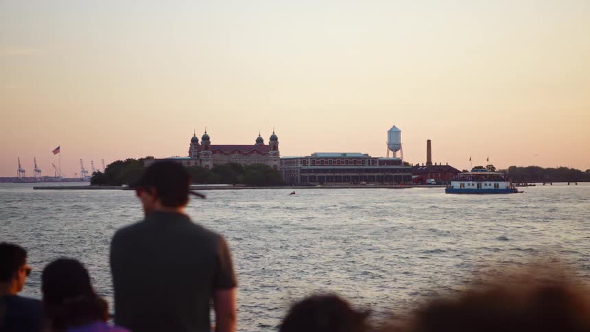 A small group of passengers look at a distant island while traveling by ferry boat across a river at dusk