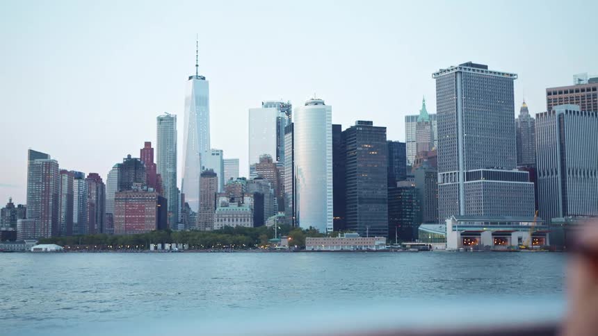 City skyline with tall buildings seen from a ferryboat traveling across the river at dusk