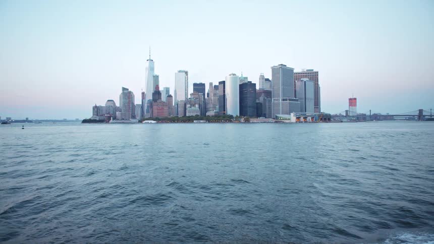 Big city skyline from a distant with multiple tall buildings and a bridge seen from sea on the horizon