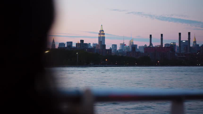 Woman looking at the empire state building in new york city from a boat at sunset
