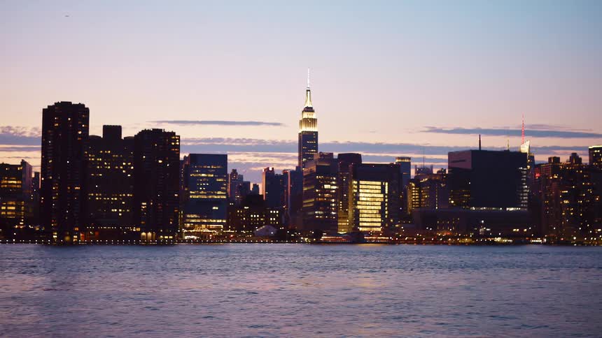 City skyline with illuminated tall buildings and skyscrapers seen from a ferryboat traveling across the river at dusk