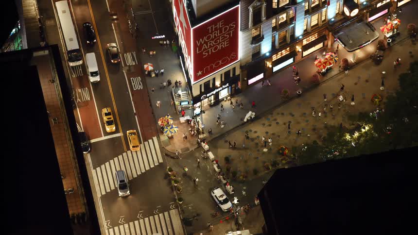Aerial view of a busy city street with pedestrians crossing a road and vehicles driving on a highway in downtown at night