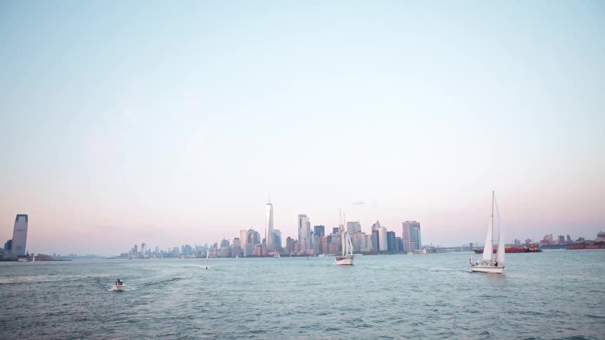 A group of boats sailing on the ocean away from a metropolis