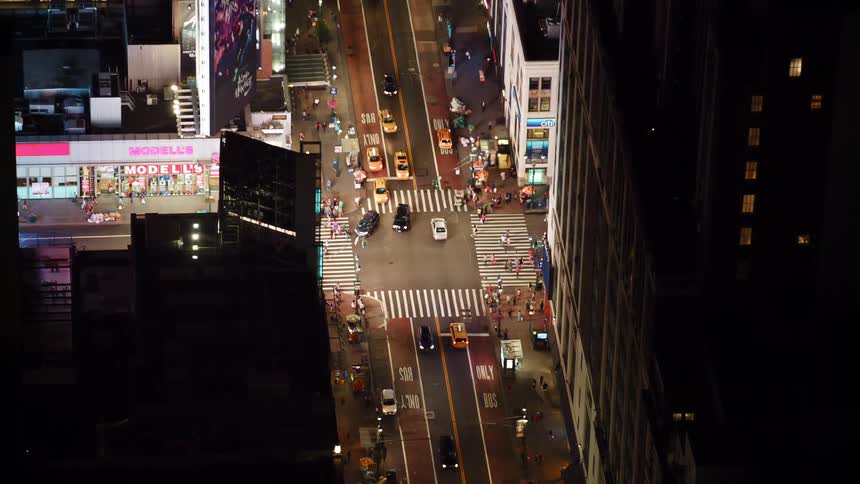 Aerial view of cars driving down a city street and people walking past stores and offices on the sidewalk