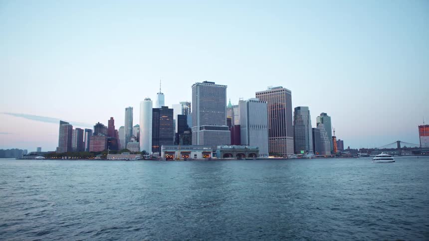City skyline with tall buildings and a bridge seen from a ferryboat traveling across the river at dusk
