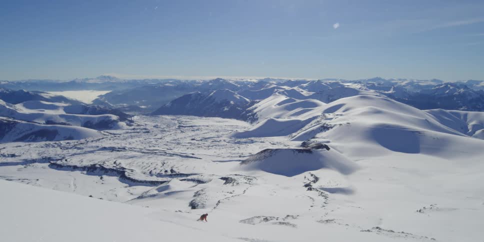 A skier flies by the camera towards a massive volcanic valley