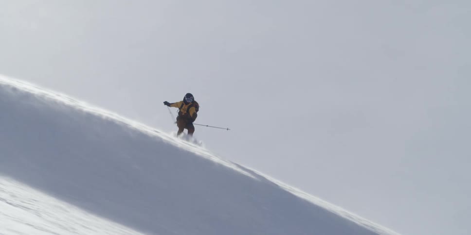 A backlit skier flips over windblown snow