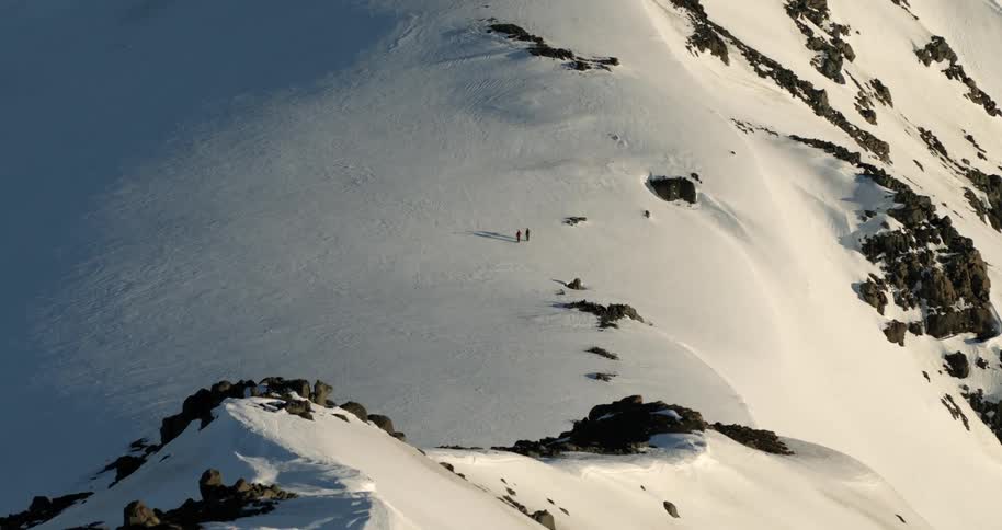 Aerial reveal of two people walking on a snowy glacier