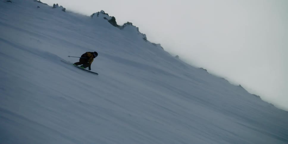 A skier flies down a windblown mountain slope