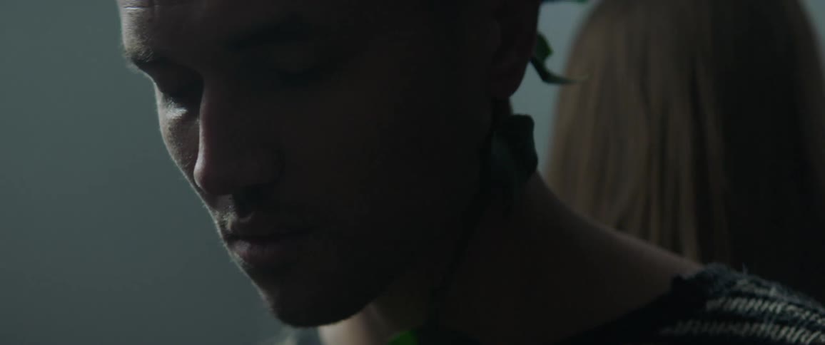 A plant vine is twisting along the neck of a man sitting behind a woman