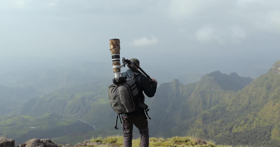 A photographer walking to the edge of a cliff in the mountains
